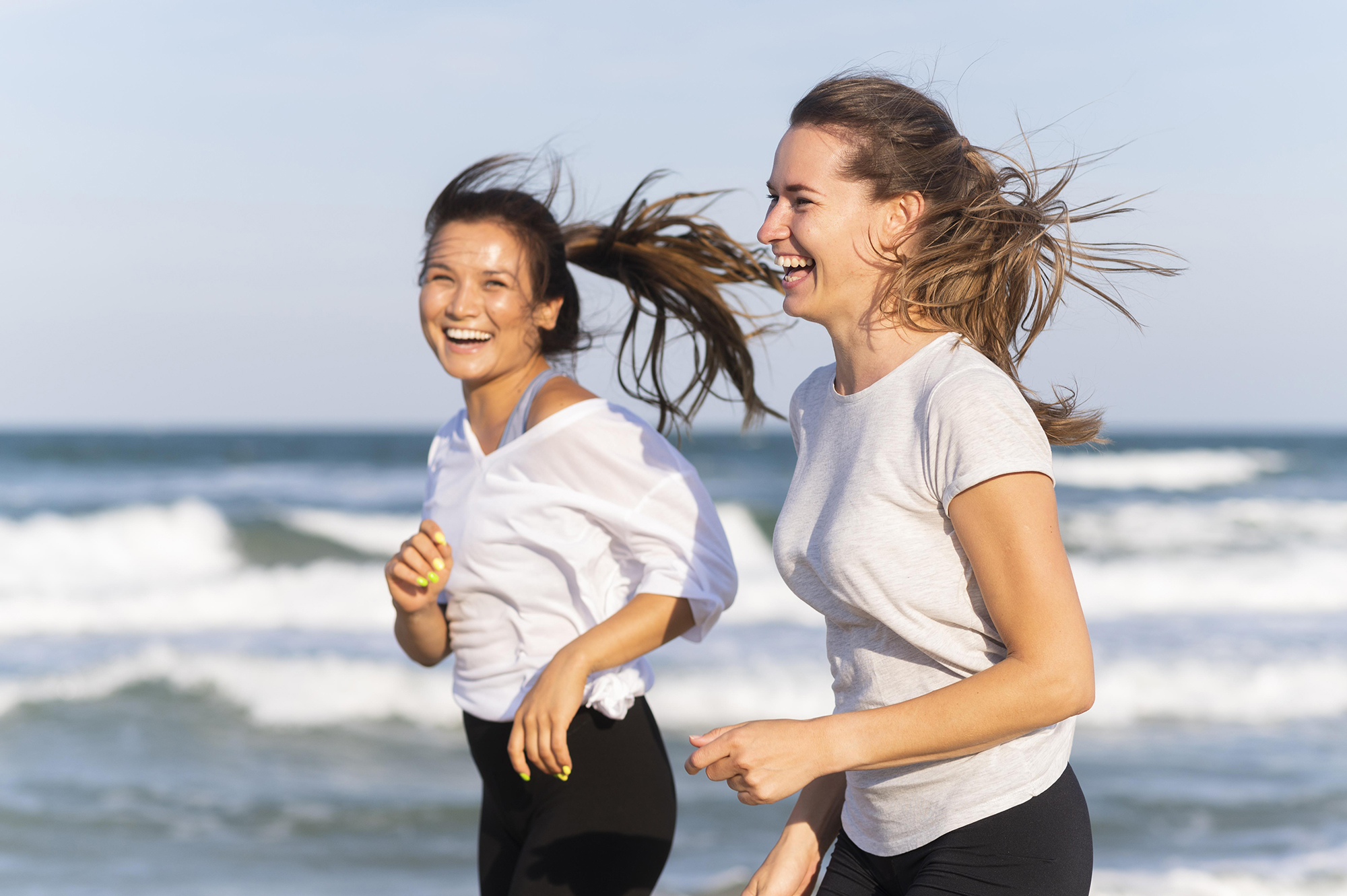Side-view-smiley-women-running-together-beach